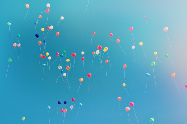 Multicolored balloons floating in a clear blue sky, symbolizing celebration and freedom.
